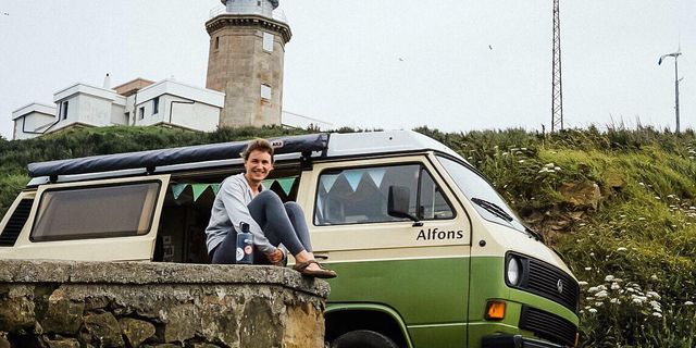 Antje vor ihrem selbst ausgebauten Camper vor einem Leuchtturm