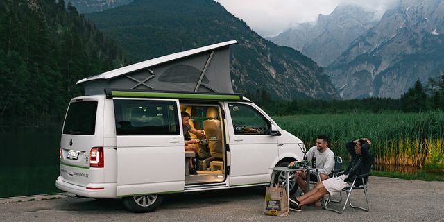 Men sitting inside and in front of a parked CamperBoys van with mountains in the background