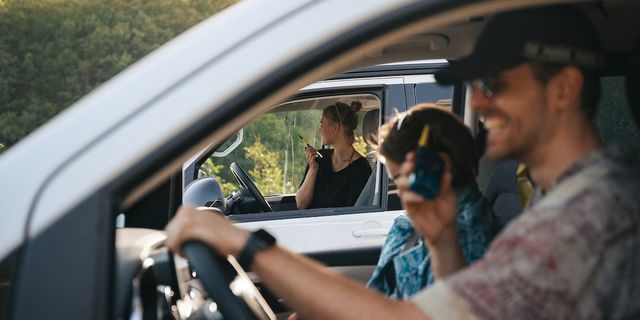 Freunde sitzen in zwei nebeneinander geparkten Vans und kommunizieren über Walkie Talkies. Sie lachen.