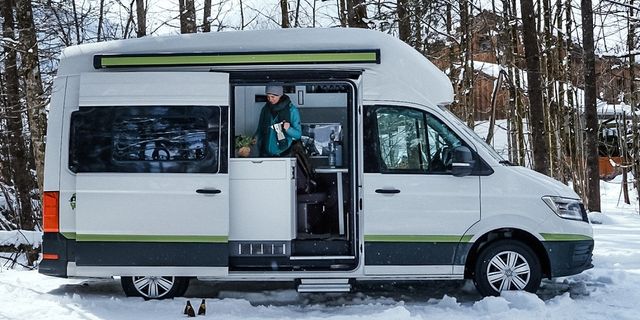 A person standing inside a CamperBoys van cooking while it is winter and there is snow outside.