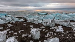 Diamond Beach als Highlight der Rundreise Island: Eisbrocken liegen im dunklen Sand am Strand, während im Hintergrund die Sonne untergeht