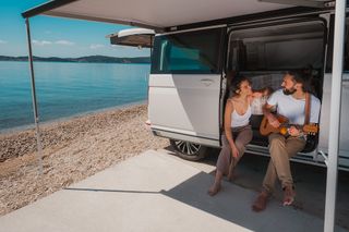 Ein Mann und eine Frau sitzen in der geöffneten Schiebetür von einem Van und sehen sich an.