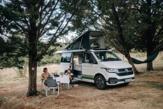 Ein Mann und eine Frau kochen an einem Campingtisch vor ihrem Camper