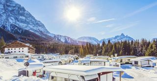 Die Sonne scheint auf das verschneite Campingresort Zugspitze. Man sieht einige Camper und eine Hütte.