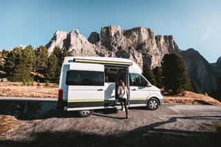 Eine Frau steigt vor einer Bergkulisse in einen CamperBoys Camper.