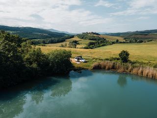 Eine Aufnahme von einem See und einem CamperBoys Camper daneben aus der Luft. Eine Frau scheint im geöffneten Camper zu sitzen.