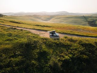 Beim Camping im Herbst steht ein Camper auf einer Landstraße zwischen grünen Wiesen.