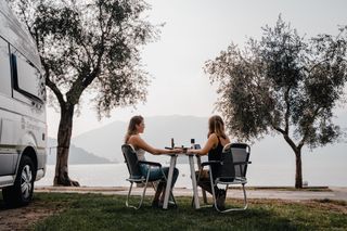 Zwei Frauen sitzen an einer Campinggarnitur vor einem VW Grand California.