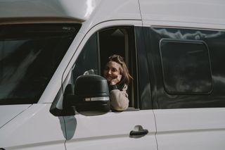 A VW Grand California camper. One of the windows is down and a woman in the drivers seat is smiling.