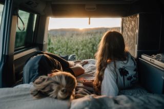 Beim Camping in Albanien liegen zwei Mädchen im geparkten Camper, die Heckklappe ist geöffnet und man sieht ein Feld.