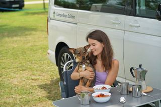 Frau mit Hund auf dem Schoß sitzt vor Camper 