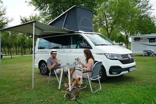 Pärchen mit Hund frühstückt unter Markise vor VW California Ocean