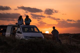 Zwei Menschen sitzen bei Sonnenuntergang auf dem Dach eines Campers.