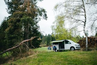 Frau sitzt unter Markise vor einem VW Ocean im Wald.