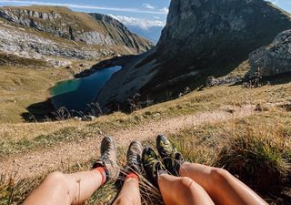 Zwei Menschen in Wanderschuhen blicken von einer Anhöhe aus auf einen Bergsee.