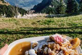 Ein Teller mit schön angerichtetem Kaiserschmarren mit grüner Bergkulisse im Hintergrund.