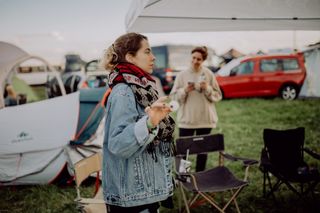 Eine Frau steht mit einem Tischtennisball auf einem Festivalgelände, um sie herum sieht man Zelte, Campingstühle und eine weitere Frau im Hintergrund. Unsere Festival Packliste findest du hier. 