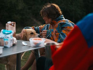 Frau beim Essen am Campingtisch mit Hund 