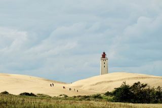 Dünenlandschaft mit Leuchtturm im Hintergrund.