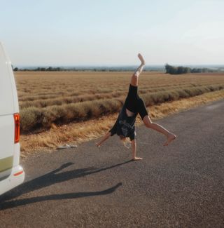 Mädchen macht Radschlag beim Camping auf Feld