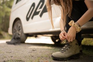 Eine Frau schnürt vor einer Wanderung beim Camping am Walchensee ihre Wanderschuhe während sie in einem Off Camper sitzt