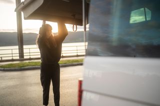 Nach dem Reinigen des Wassertanks ihres Wohnmobils macht eine junge Frau bei Sonnenuntergang die Heckklappe zu.