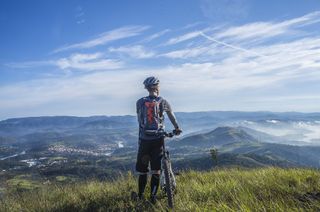 Ein Fahrradfahrer steht in den Bergen und schaut sich das Panorama an.