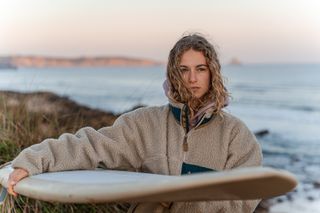 Eine Frau mit einem Surfbrett unter dem Arm steht am Strand.