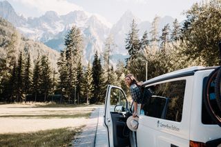 Woman in VW California Ocean in front of mountain panorama