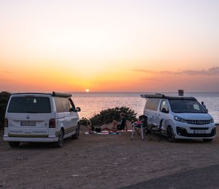 Zwei Menschen beim Yoga zwischen ihren Campern am Meer